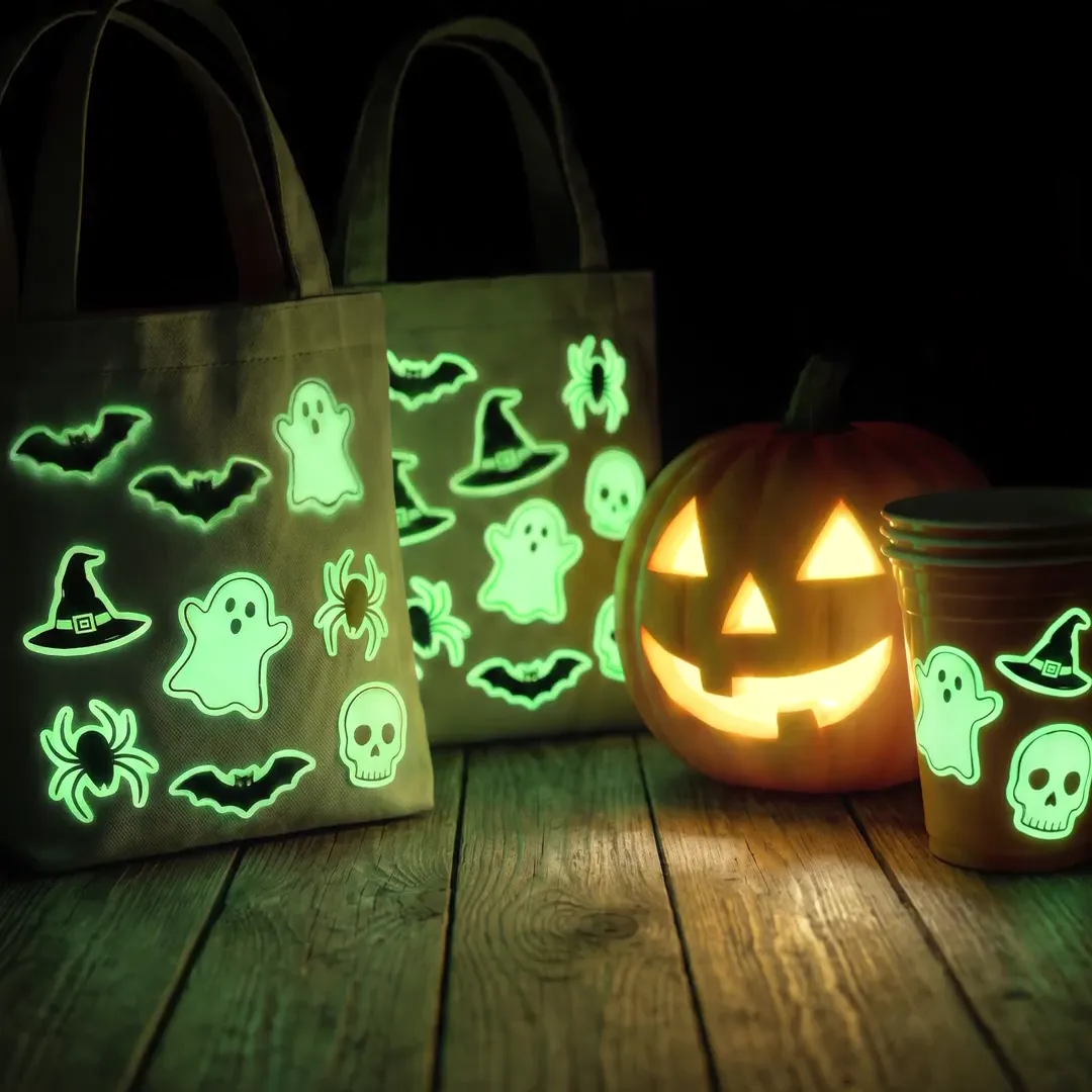 Bolsas de dulces, calabaza y vaso con stickers fotoluminiscentes que brillan en verde; detrás, una bruja ríe con un sticker de Calcaprint en la mano
